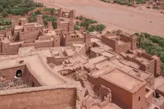 Mud-brick kasbahs of Aït Benhaddou seen from above, with palms along the riverbed